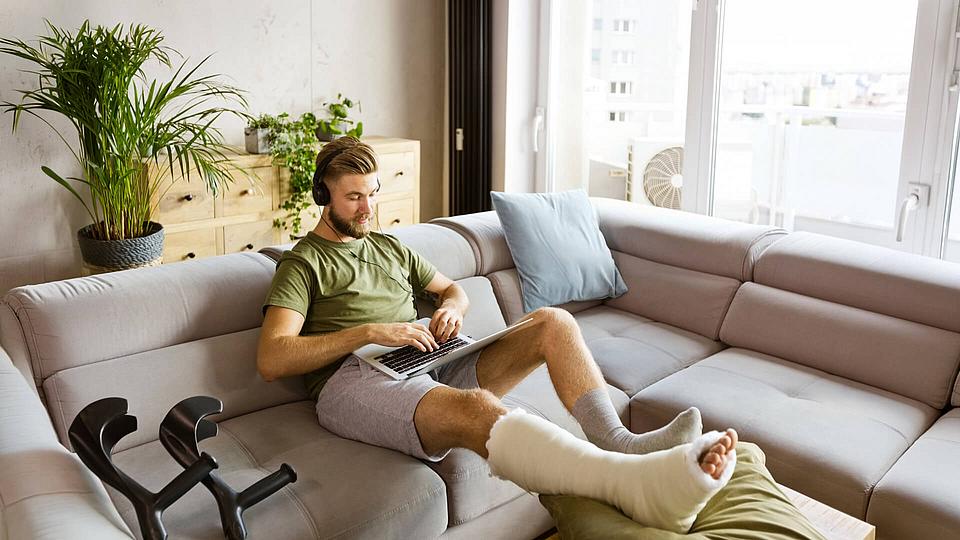 Mann sitzt mit gegipsten Bein auf dem SOfa