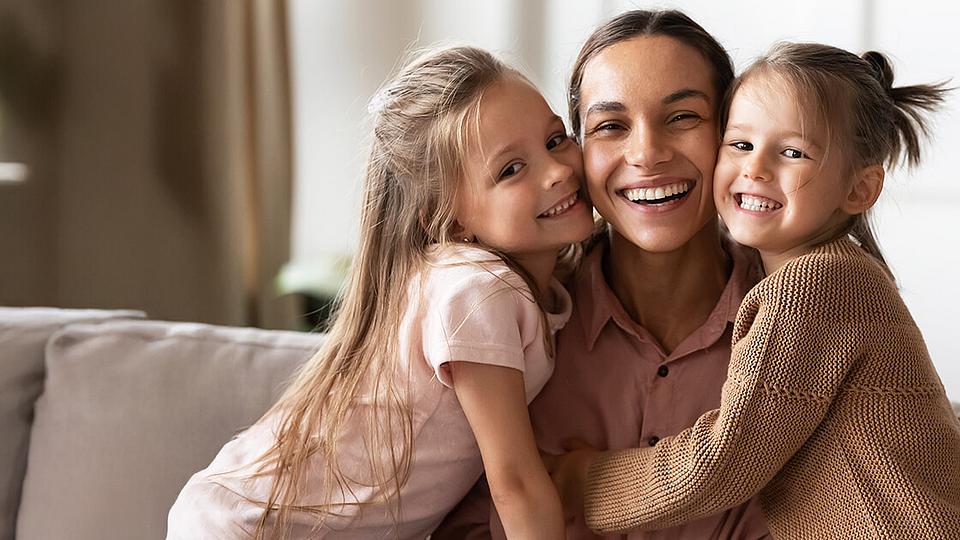 Eine Mutter, die ihre beiden Töchter im Arm hält. 
