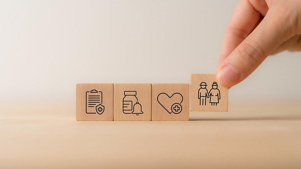 Hand hält Holzwürfel mit Symbolen im Zusammenhang mit der Gesundheitsversorgung.