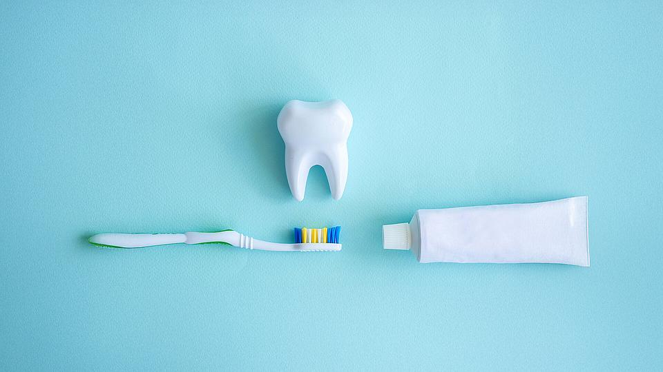 Großer Plastikzahn, Bürste und Zahnpasta auf blauem Hintergrund.