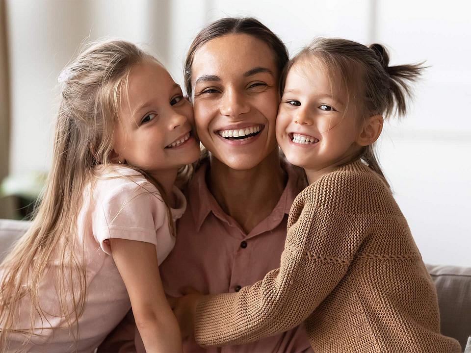 Eine Mutter, die ihre beiden Töchter im Arm hält. 