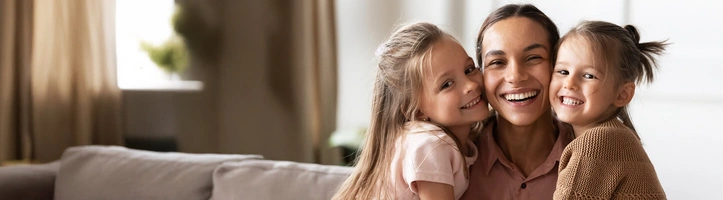 Eine Mutter, die ihre beiden Töchter im Arm hält. 