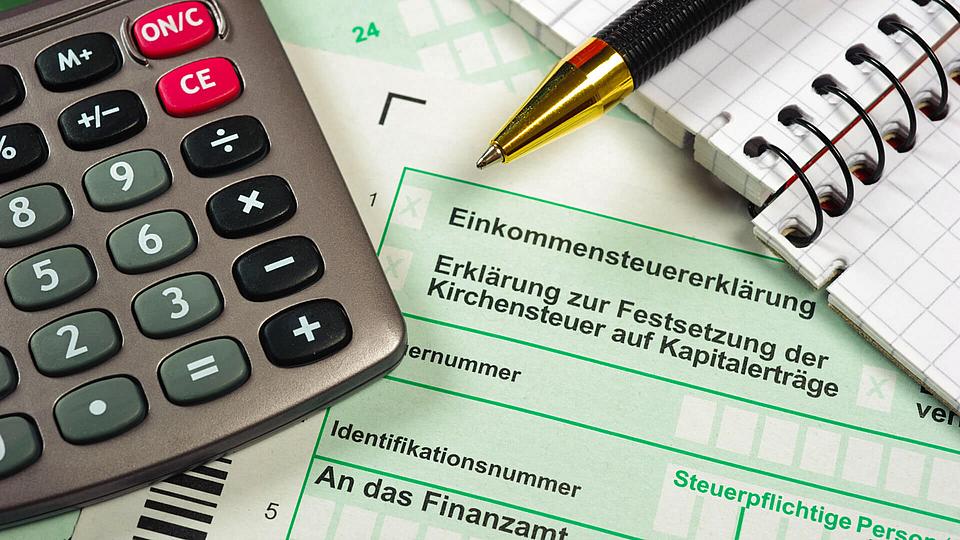 Taschenrechner mit Notizblock und Kugelschreiber liegen auf Dokumenten zur Steuererklärung