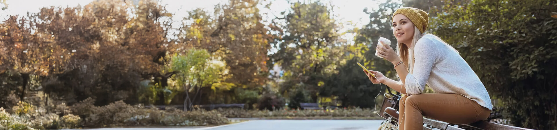 Junge Frau auf einer Bank mit Kaffee und Smartphone Junge Frau auf einer Bank mit Kaffee und Smartphone