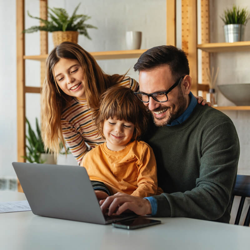 Mann sitzt mit zwei Kindern vor einem Laptop, alle lächeln und schauen auf den Bildschirm Mann sitzt mit zwei Kindern vor einem Laptop, alle lächeln und schauen auf den Bildschirm