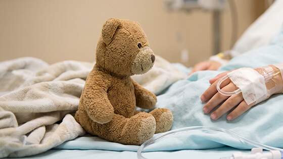 Kind liegt im Krankenhausbett mit Kuscheltier