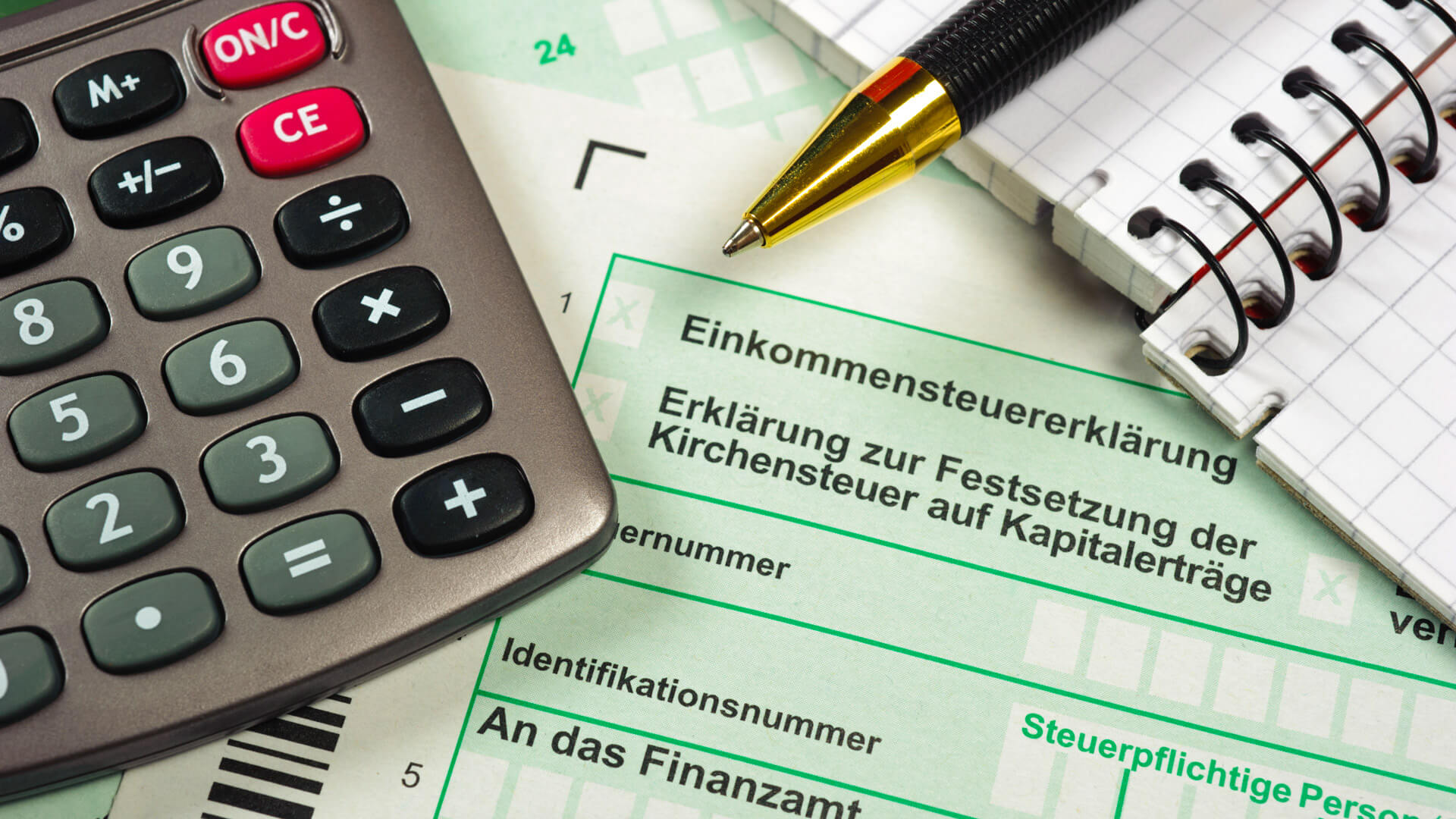 Taschenrechner mit Notizblock und Kugelschreiber liegen auf Dokumenten zur Steuererklärung