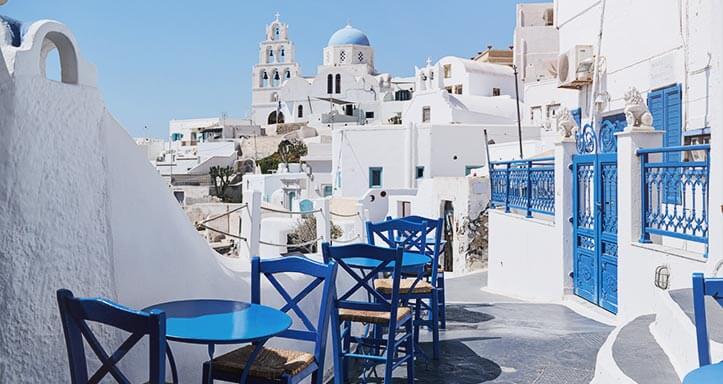 Blaue Tische und Stühle zwischen den weißen Häusern von Santorini Blaue Tische und Stühle zwischen den weißen Häusern von Santorini