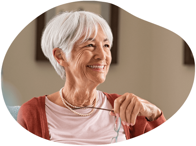 Eine Seniorin hat eine Brille in der Hand und lächelt.