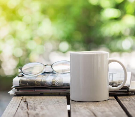 Kaffeetasse, Brille und Zeitung auf einem Holztisch Kaffeetasse, Brille und Zeitung auf einem Holztisch