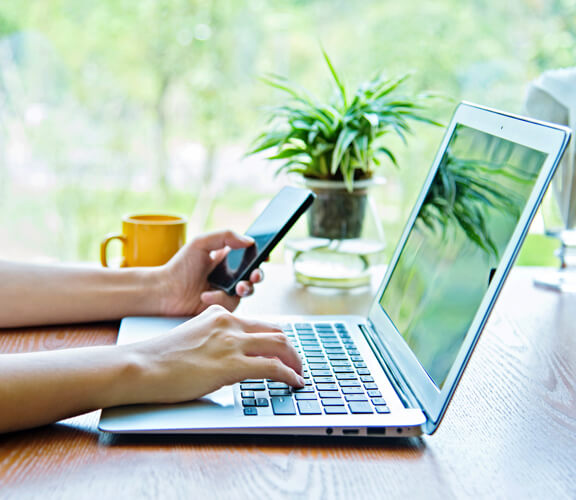Arme einer Person, die gleichzeitig am Laptop und Smartphone arbeitet Arme einer Person, die gleichzeitig am Laptop und Smartphone arbeitet
